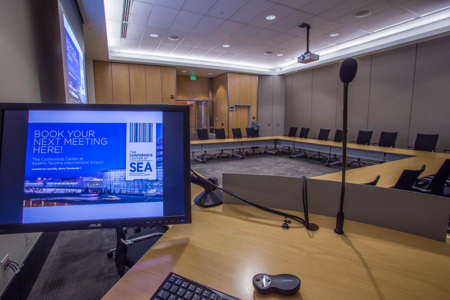 View from the podium located inside the Amsterdam Conference room featuring a hollow square room set with the projector and dropdown screen