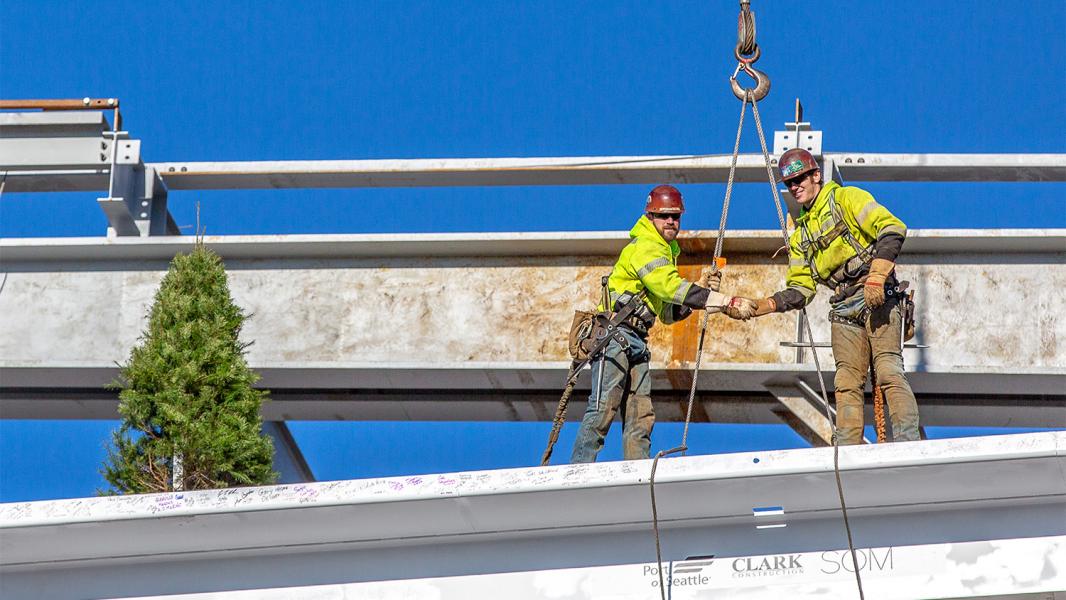 Tradesmen shake hands after guiding the final beam into place on the International Arrivals Facility at Sea-Tac Airport December 4, 2018