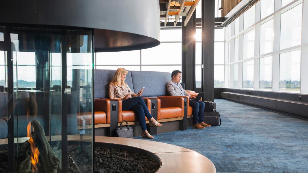 Two travelers sitting inside the Alaska Lounge working on their devices