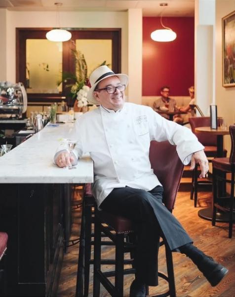 A photo of the Chef in the Hat, perched on a bar stool and leaning against a white marble countertop