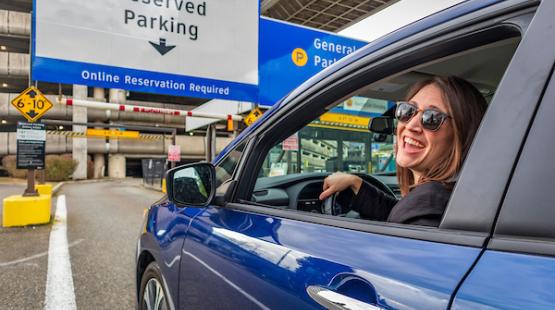 A woman is smiling while driving a blue car into the parking garage.