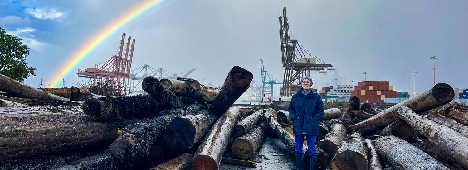 George Blomberg at a Port habitat site with a rainbow and cargo terminal in the background.