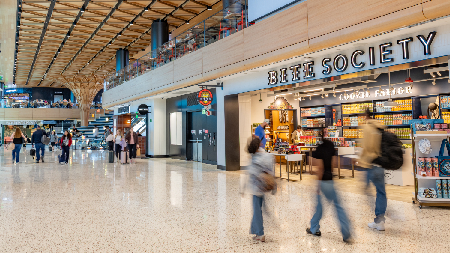 Travelers walk through the new C Concourse Expansion area in SEA Airport, with the Bite Society storefront shown in the background