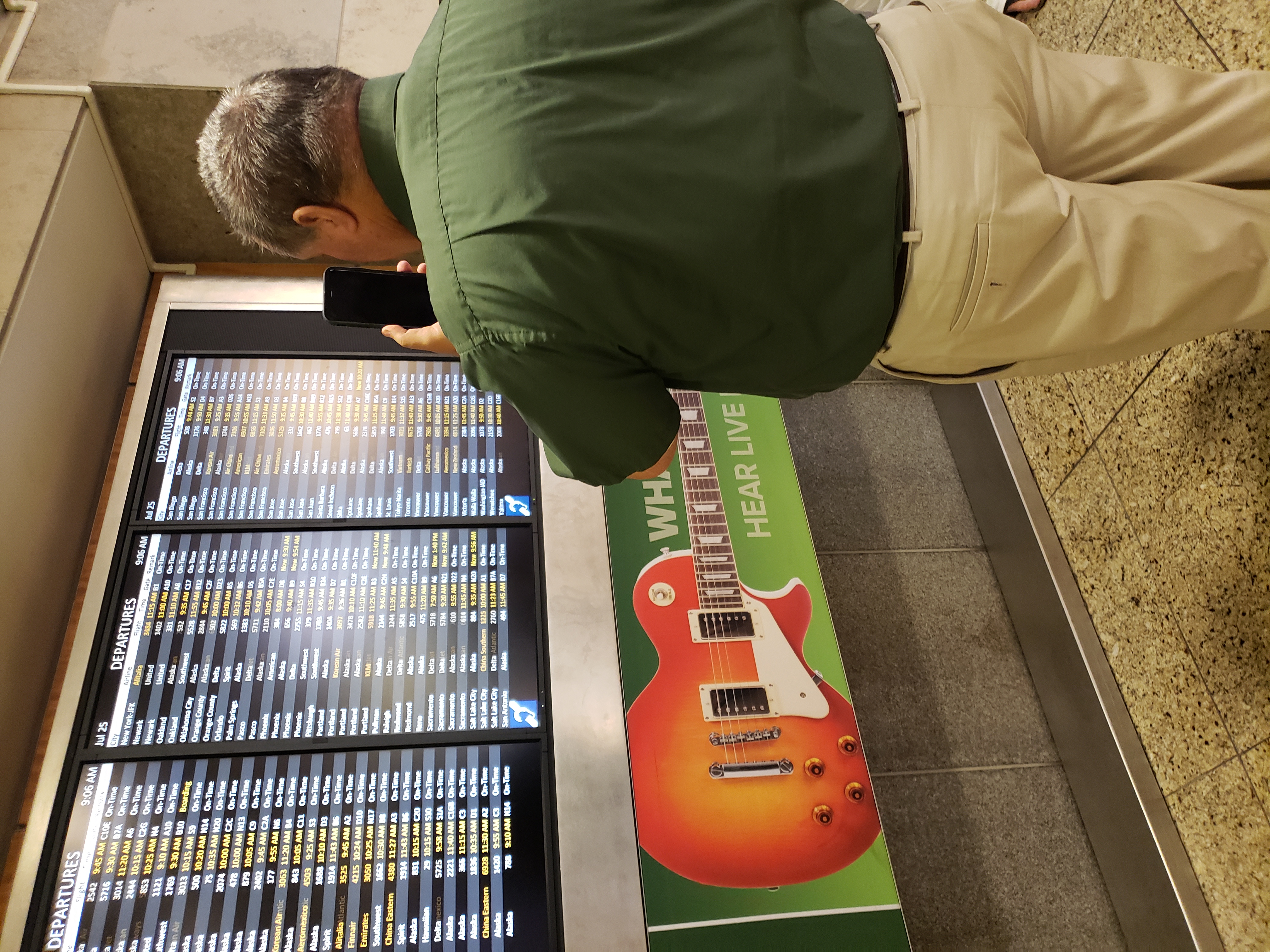 A man holding a cell phone up to an airport departures board