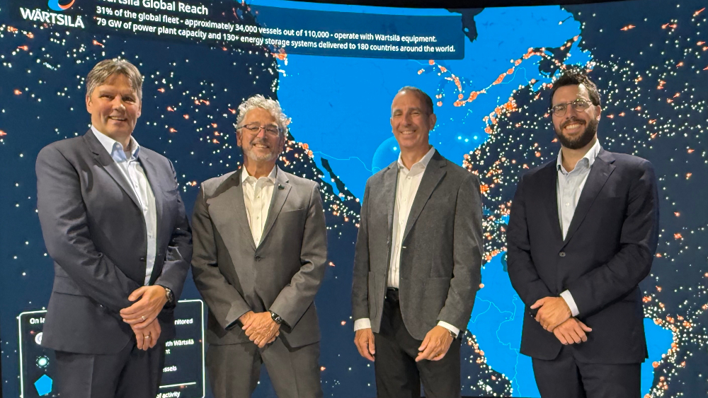Vesa Koivumaa, head of strategic growth at Wartsila; Commissioner Felleman; Patrick Gallagher, executive director of the Marine Exchange of Puget Sound; and Jim Mumford, strategic advisor to the Commission Office, standing in front of a map showing the positions of tens of thousands of vessels operating with Wartsila equipment around the world