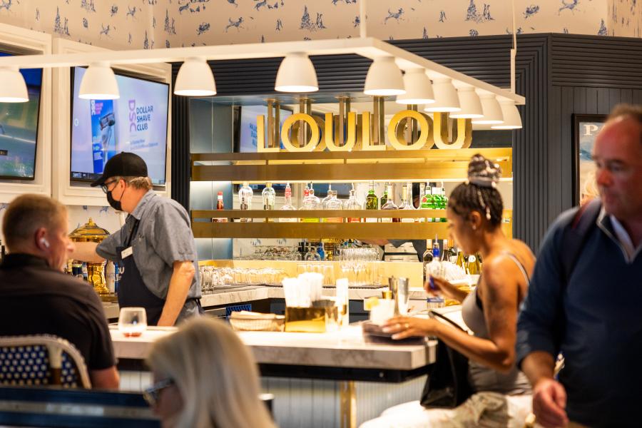 A photo of the bar at LouLou, a bartender prepares drinks while travelers sit around the countertop