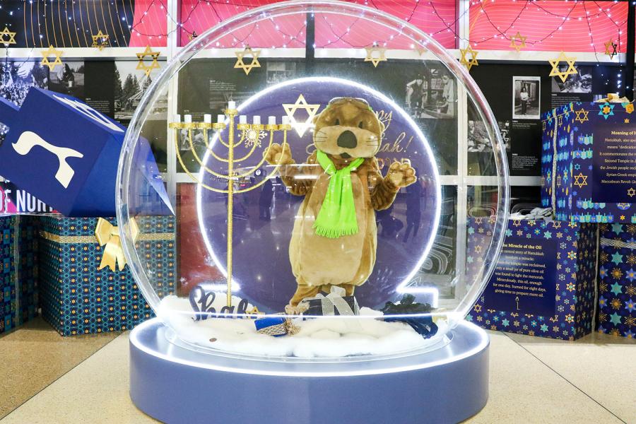 Image of Jett the S-E-A Otter enjoying the interactive snow globes holiday decorations at S-E-A Airport.