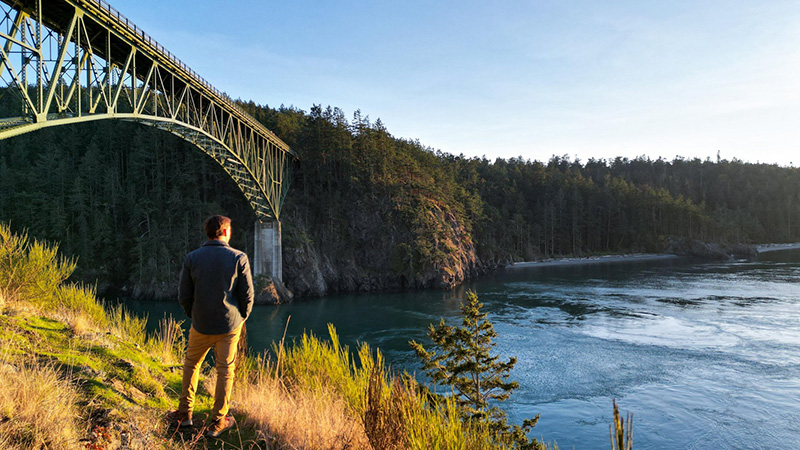 A man stands under the Deception Pass Bridge