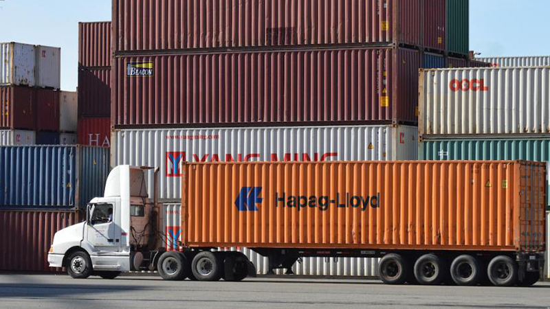 A drayage truck in the foreground with shipping containers in the background