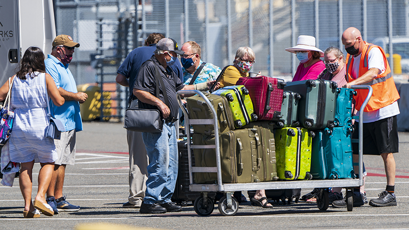 Cruise passengers surround a dock worker shuttling a full baggage cart across Smith Cove Cruise Teminal in Seattle July 19 2021