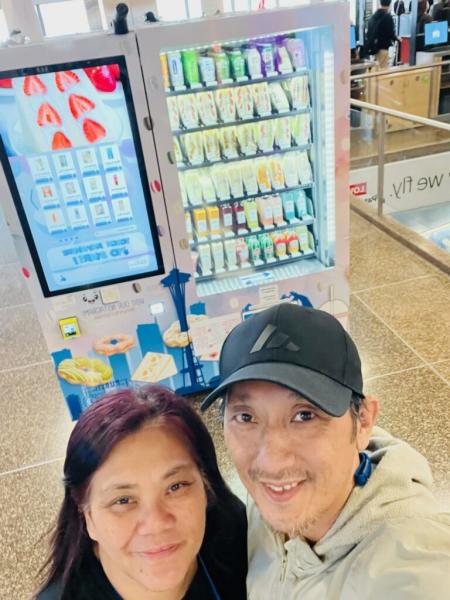 Photo of Daniel and Eunice in front of their vending machine