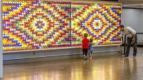A large, brightly colored geometric wall display made of circular elements, with an adult and two children looking closely at it.