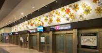 Airport train platform with colorful flower‑shaped glass art above the doors.