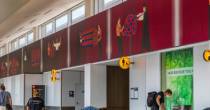 Airport concourse wall featuring a long mural of figures interacting with bold geometric shapes.