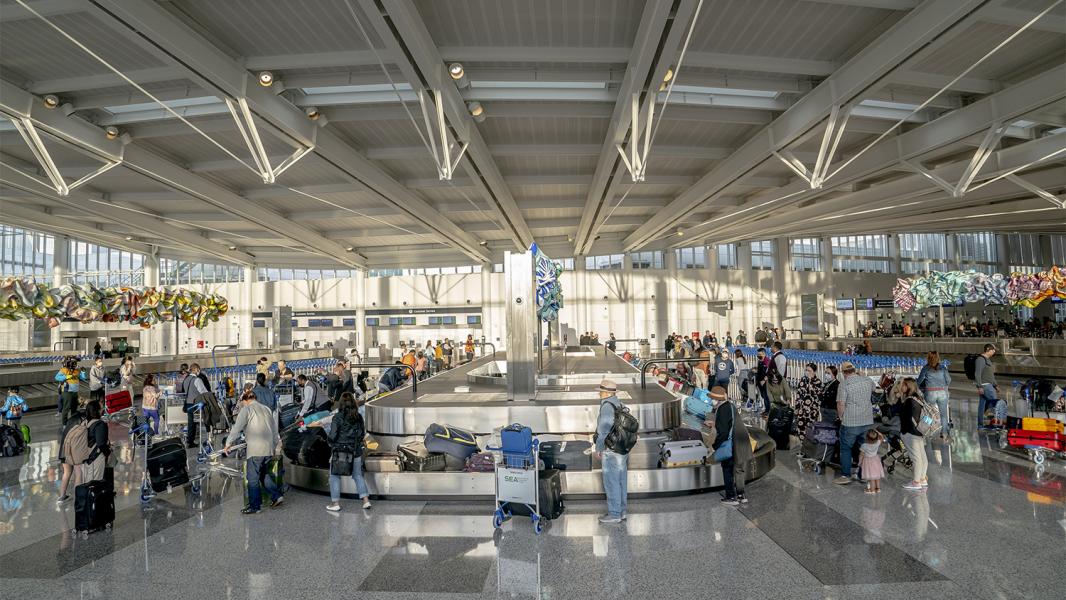 Passengers milla round the baggage claim in the open, light-filled grand hallway of the new IAF at SEA Airport