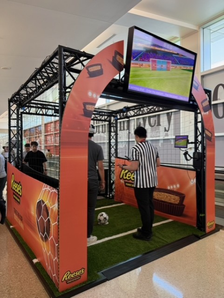 Virtual soccer simulator with two people inside, one wearing a referee uniform, and the other approaching a soccer ball