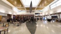 A large indoor airport space features a suspended leaf‑shaped sculpture hanging from the ceiling above a seating and dining area.