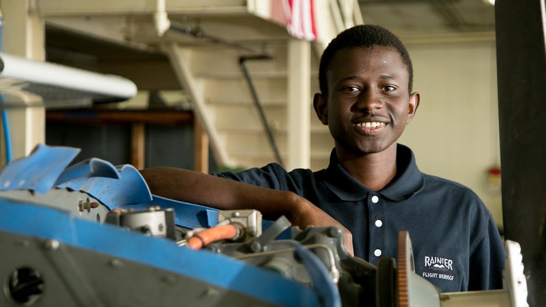 Youth intern stands in uniform in front of maintenance machinery at Rainier Flight 