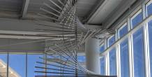 A suspended metal sculpture made of curved, radiating rods hangs near tall windows in an airport concourse.
