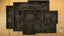 A dark, multi-panel wall sculpture made of geometric, layered shapes hangs on a pegboard wall.