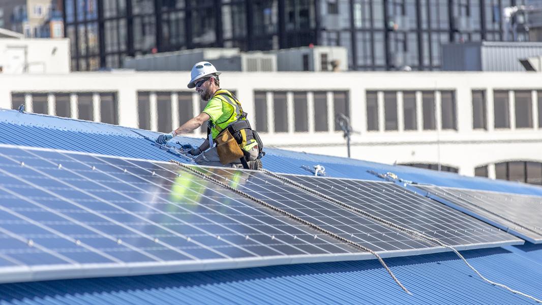 Engineer instals solar panels on the blue metal roof of Pier 69 Port headquarters building