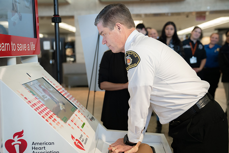 Port of Seattle Fire Chief Randy Krause demonstrates Hands-Only CPR training kiosk at SEA Airport.