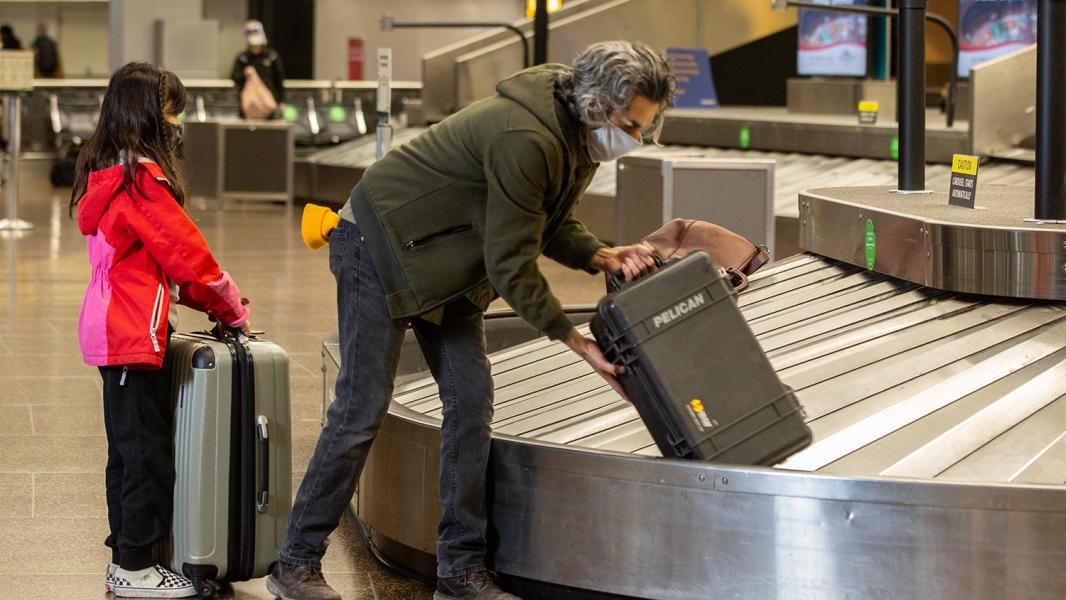 Father and daughter collect baggage from a carousel at sEA Airport in a largely empty terminal during, Nov. 2020