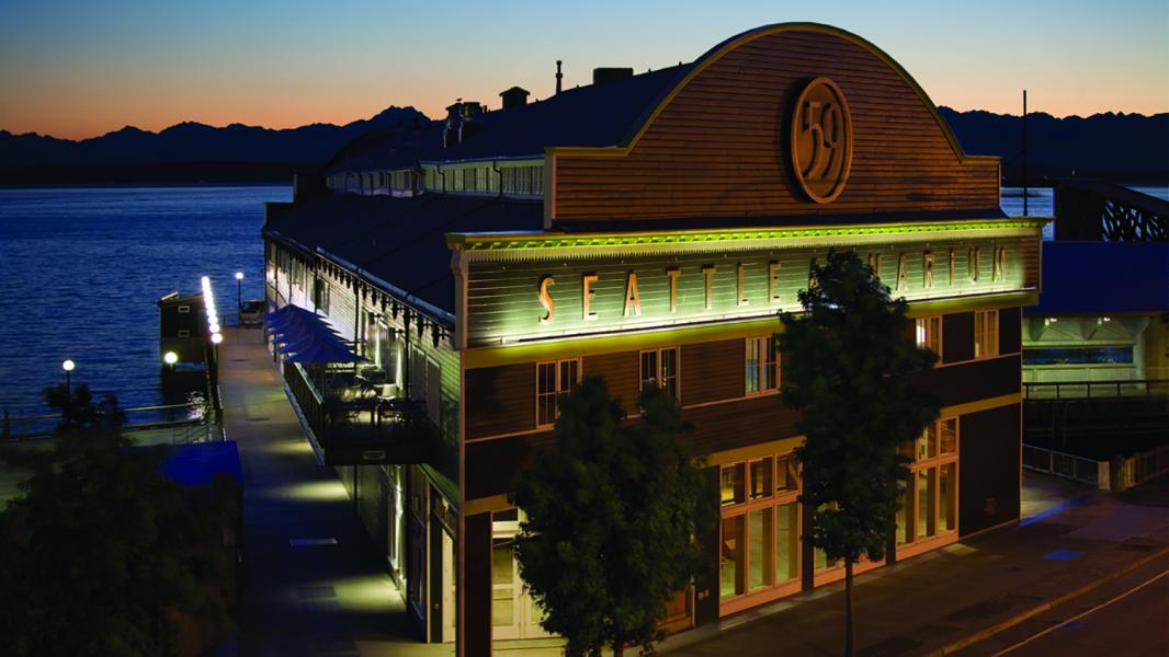 Facade of the seattle Aquarium on the waterfront in front of an orange sunset and purple Olympic Mountains