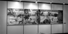 A large wall-mounted artwork with fragmented, mirrored images is displayed above lounge seating in a gallery-like space.