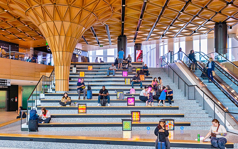 Travelers sit along side art boxes on the Grand Stairs of the C Concourse Expansion