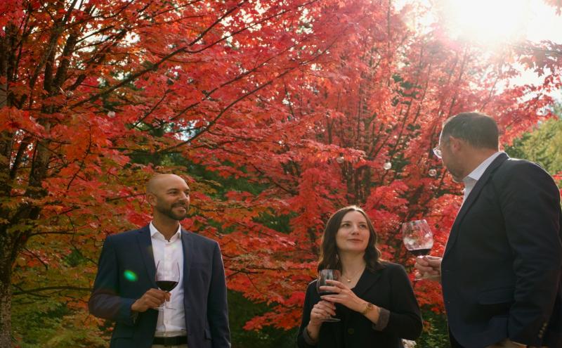 Three people wine tasting with a backdrop of fall foliage.
