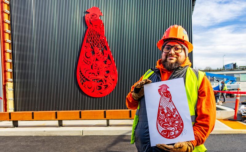 Ty Juvinel poses in the foreground with his piece "Beach Seining" on the Maritime Innovation Center building.