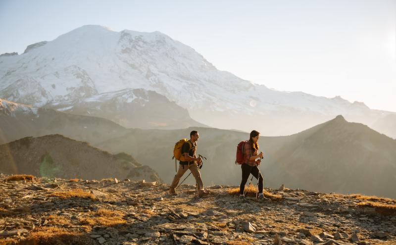 two hikers during sunset on a trail with a snowy mountain behind them