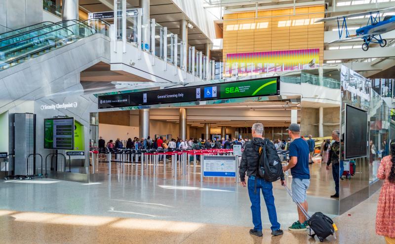 Two travelers walk towards Checkpoint 1, one with roller bag carry-on