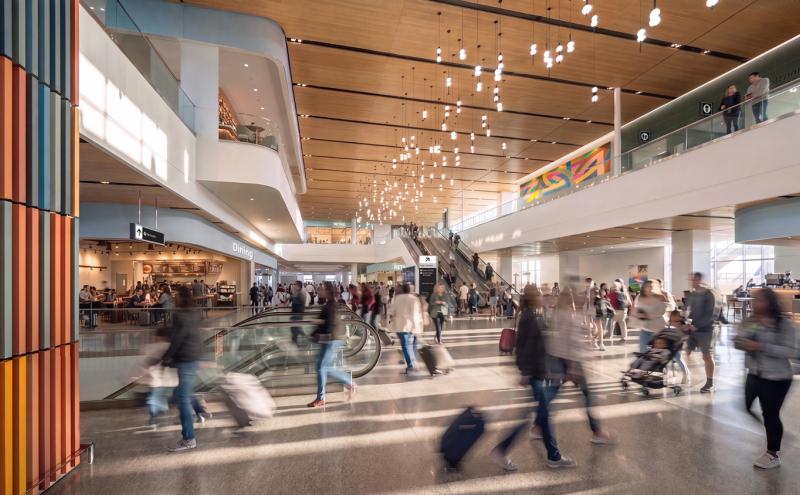 Rendering of the future S Concourse Evolution Project at Seattle-Tacoma International Airport, showcasing a modern terminal with wooden ceilings, dining areas, and people moving through a busy concourse