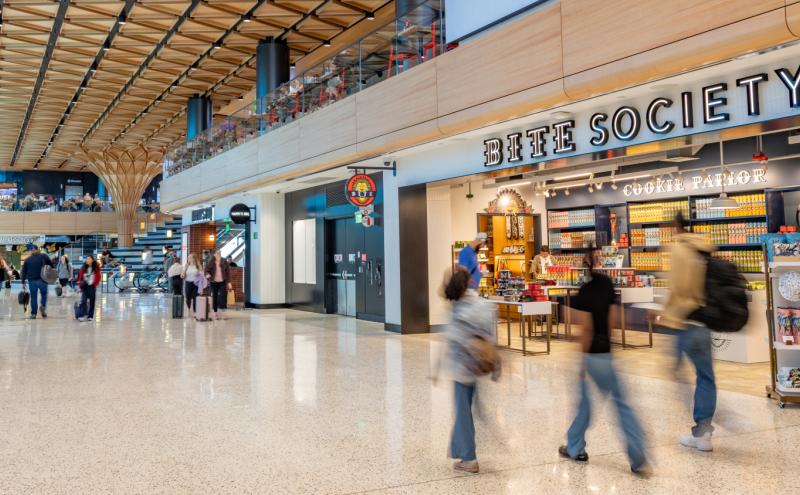 Travelers walk through the new C Concourse Expansion area in SEA Airport, with the Bite Society storefront shown in the background