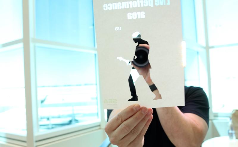 Artist Rudy Willingham holds a paper cut out in front of camera lens in the C Concourse