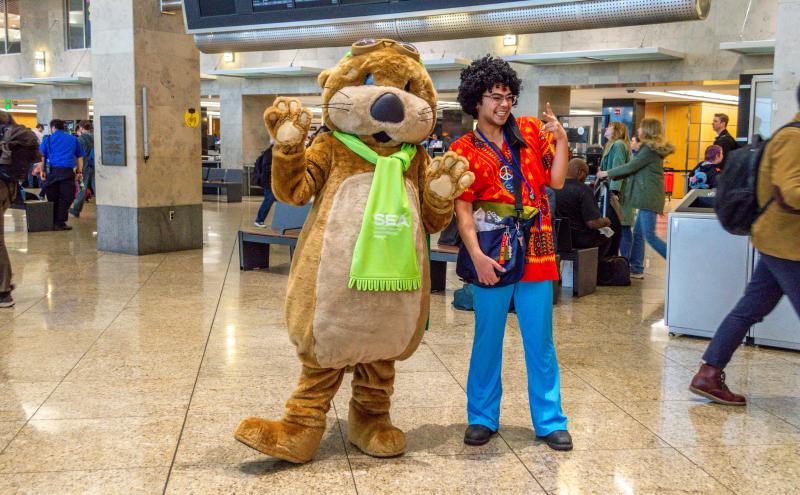 Jett the SEA Otter and person dressed in hippie costume pose in the terminal