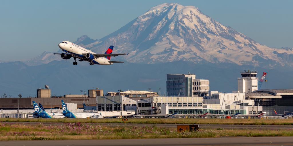 A commercial jet takes off from SEA Airport, with Mt. Rainier in the background