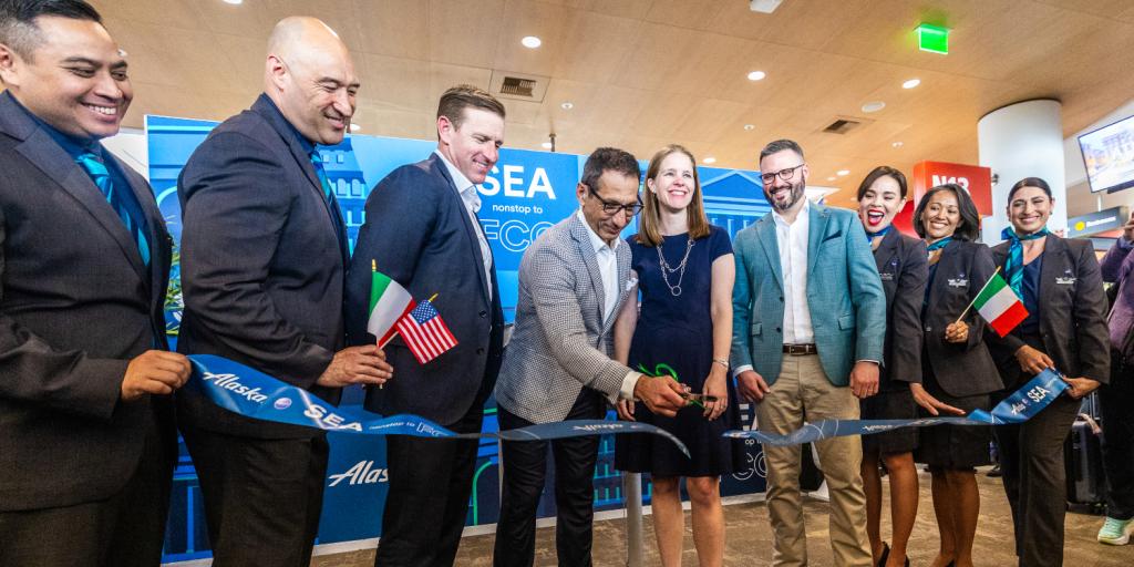 Alaska Airlines flight crew stand in a line smiling and holding Italian and United States of America flags, recognizing the new connection between the two destinations from SEA Airport. 