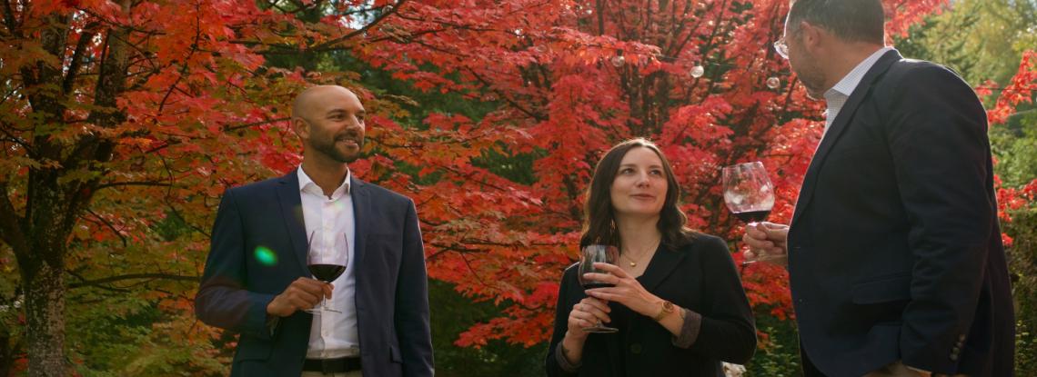 A group of people sipping wine with fall foliage in the background.