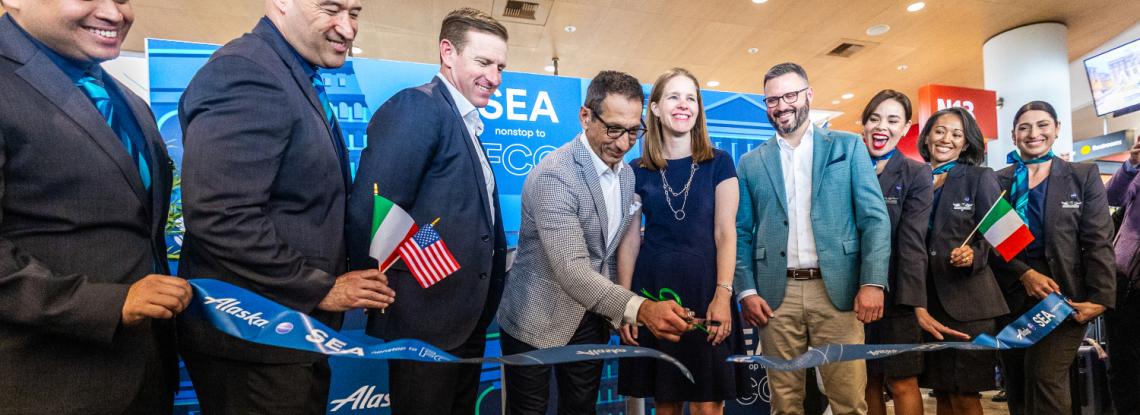 Alaska Airlines flight crew stand in a line smiling and holding Italian and United States of America flags, recognizing the new connection between the two destinations from SEA Airport. 