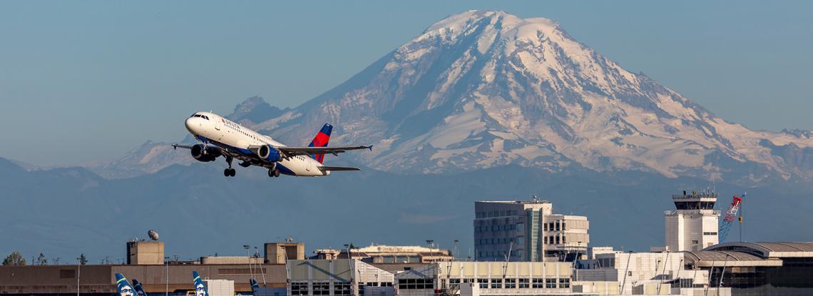 A commercial jet takes off from SEA Airport, with Mt. Rainier in the background
