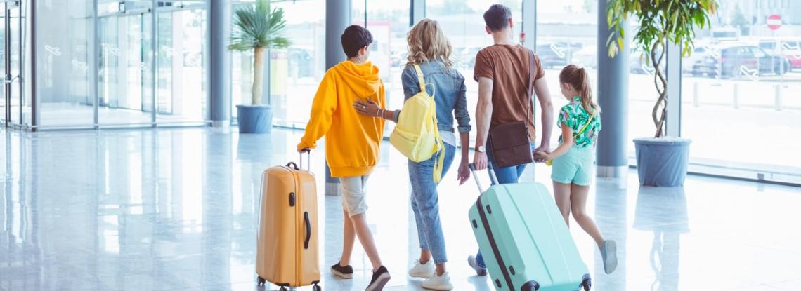 Family of four walking through airport with luggage.