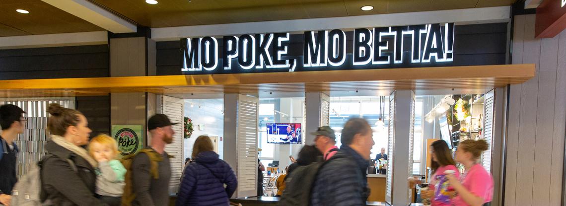Travelers walk by Poke to the Max on the D Concourse.