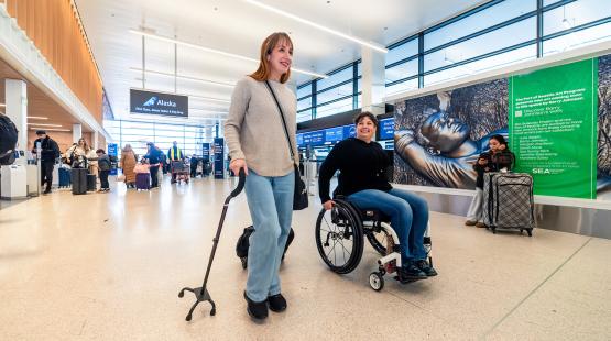 A traveler using a cane and traveler in a wheelchair walk through the terminal at SEA.