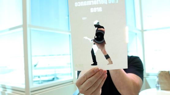 Artist Rudy Willingham holds a paper cut out in front of camera lens in the C Concourse