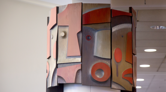 Two sides of the sculpture showing the wooden pieces projecting outward at different depths, giving the mask forms physical relief. 