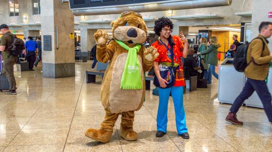 Jett the SEA Otter and person dressed in hippie costume pose in the terminal