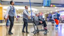 Employees push a woman through SEA in a wheelchair. Potot taken July 2019. Don Wilson photographer.